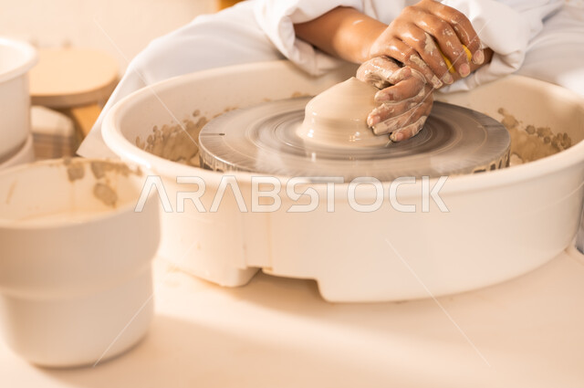 حرف وصناعات يدوية شعبية من التراث السعودي العريق، العمل في صناعة الخزفيات, اواني خزفية مصنوعة من الطين، صنع الجرار الفخارية المزخرفة، صورة مقربة لايدي امرأة عربية سعودية خليجية تقوم بصناعة الفخار