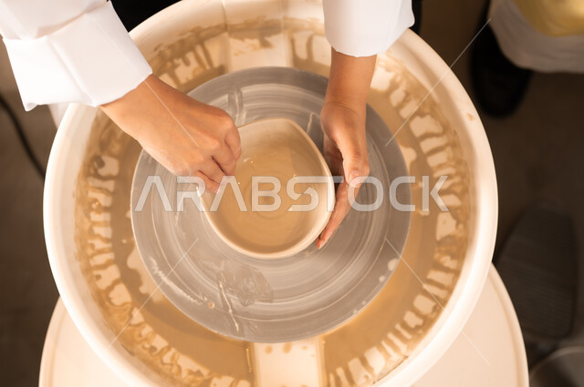 حرف وصناعات يدوية شعبية من التراث السعودي العريق، العمل في صناعة الخزفيات, اواني خزفية مصنوعة من الطين، صنع الجرار الفخارية المزخرفة، صورة مقربة لايدي امرأة عربية سعودية خليجية تقوم بصناعة الفخار