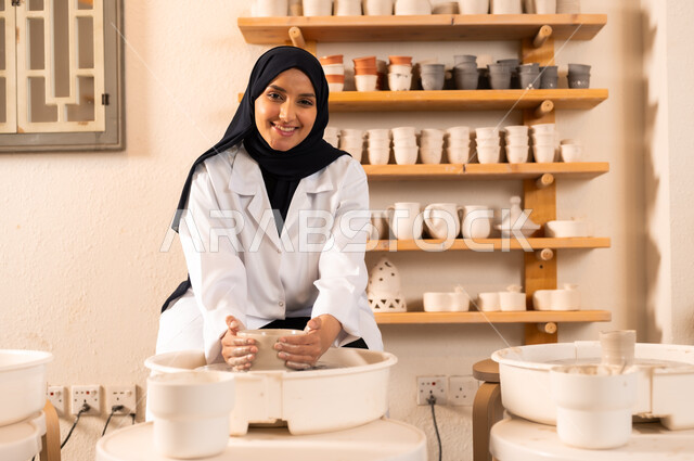 العمل في صناعة الخزفيات، صنع الجرار الفخارية المزخرفة، حرف وصناعات يدوية شعبية من التراث السعودي العريق, اواني خزفية مصنوعة من الطين، صورة مقربة لشابة عربية خليجية سعودية مبتسمة تقوم بصنع الفخار