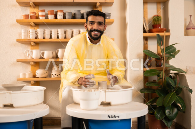 A Saudi Gulf Arab professional works in an artistic workshop, practicing the skill of making pottery, professionally coloring ceramics and pottery, Saudi handicrafts.
