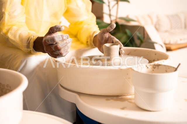محترف عربي سعودي خليجي يعمل في ورشة الاعمال الفنية، ممارسة مهارة صنع الفخار، احتراف تلوين الخزف والفخاريات، أعمال يدوية سعودية، صوره مقربة لايدي حرفي يقوم بصنع الفخار