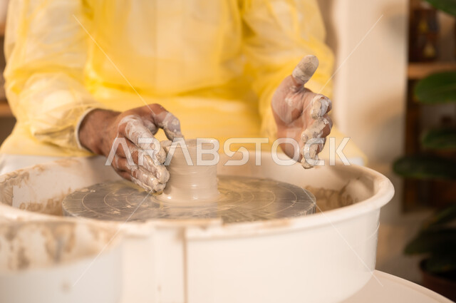 محترف عربي سعودي خليجي يعمل في ورشة الاعمال الفنية، ممارسة مهارة صنع الفخار، احتراف تلوين الخزف والفخاريات، أعمال يدوية سعودية، صوره مقربة لايدي حرفي يقوم بصنع الفخار