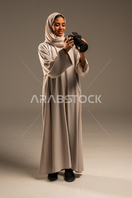 Saudi women's jobs and professions, professional photography using high-resolution digital cameras, portrait of a Saudi Arabian Gulf woman wearing a hijab and abaya taking souvenir photos using a photographic camera, full-length body image, gray background