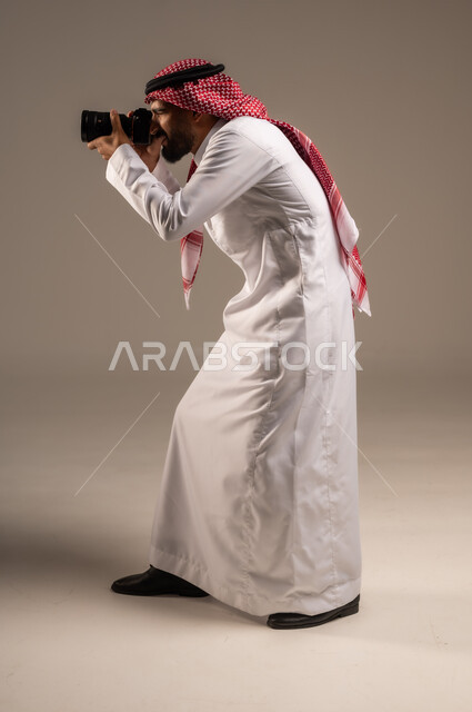 Mastering and professionalizing the profession of photography, side portrait of a Saudi Arabian Gulf man wearing a traditional shemagh and thobe taking souvenir photos with a photographic camera, using high-resolution digital cameras, Saudi jobs and professions, full-length body image, gray background