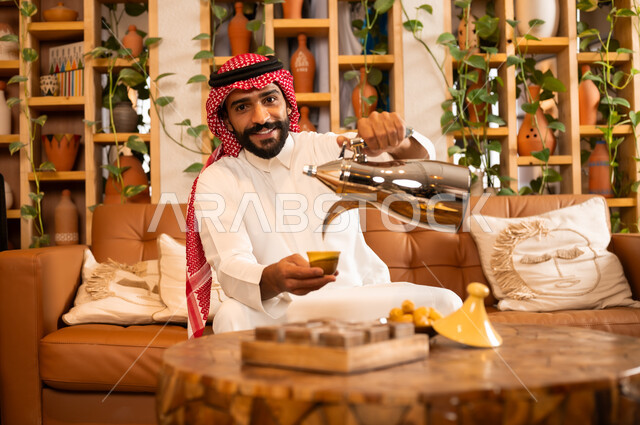 عادات وتقاليد أصيلة في تقديم المشروبات, السير على نهج الأجداد في إكرام الضيف, صورة مقربة لرجل عربي خليجي سعودي يرتدي الثوب التقليدي والشماغ يقوم بصب القهوة من الدلة النحاسية, توارث حسن الاستقبال والكرم, تقديم المنتجات المحلية للضيوف