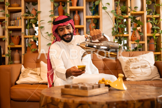 عادات وتقاليد أصيلة في تقديم المشروبات, السير على نهج الأجداد في إكرام الضيف, صورة مقربة لرجل عربي خليجي سعودي يرتدي الثوب التقليدي والشماغ يقوم بصب القهوة من الدلة النحاسية, توارث حسن الاستقبال والكرم, تقديم المنتجات المحلية للضيوف