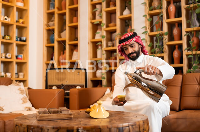 عادات وتقاليد أصيلة في تقديم المشروبات, السير على نهج الأجداد في إكرام الضيف, صورة مقربة لرجل عربي خليجي سعودي يرتدي الثوب التقليدي والشماغ يقوم بصب القهوة من الدلة النحاسية, توارث حسن الاستقبال والكرم, تقديم المنتجات المحلية للضيوف