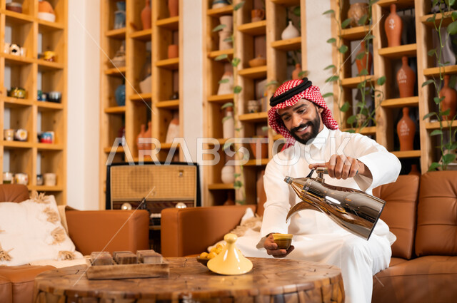 عادات وتقاليد أصيلة في تقديم المشروبات, السير على نهج الأجداد في إكرام الضيف, صورة مقربة لرجل عربي خليجي سعودي يرتدي الثوب التقليدي والشماغ يقوم بصب القهوة من الدلة النحاسية, توارث حسن الاستقبال والكرم, تقديم المنتجات المحلية للضيوف