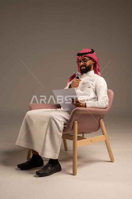 قراءة الملاحظات والمعلومات، بورتريه لرجل عربي خليجي سعودي يرتدي الثوب التقليدي والشماغ يجلس على الكرسي يحمل بيده مجموعة من الأوراق ومكبر الصوت يقوم بإلقاء الخطابات، القيام بالحوارات والنقاشات، إعداد وتحضير أفكار الخطاب بشكل مسبق، خلفية رمادية