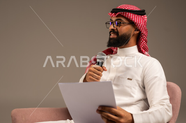 إعداد وتحضير أفكار الخطاب بشكل مسبق، القيام بالحوارات والنقاشات، بورتريه مقرب لرجل عربي خليجي سعودي يرتدي الثوب التقليدي والشماغ يجلس على الكرسي يحمل بيده مجموعة من الأوراق ومكبر الصوت يقوم بإلقاء الخطابات، قراءة الملاحظات والمعلومات، خلفية رمادية