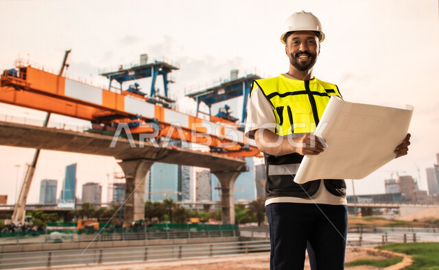 Study of the basics of the construction plan, work in the engineering sector, a Saudi Arabian Gulf engineer wearing a protective vest and helmet holding construction plans in his hands, reviewing and presenting project manuscripts in full, project management and follow-up, the concept of architectural engineering and construction
