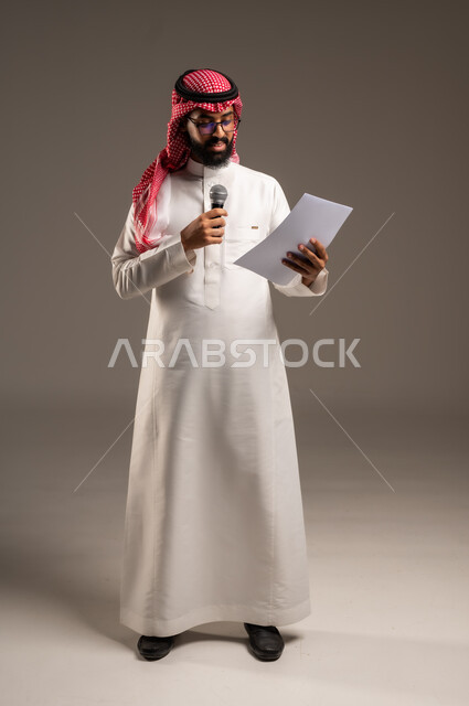 Reading notes and information, conducting dialogues and discussions, portrait of a Saudi Arabian Gulf man wearing traditional thobe and shemagh holding a bunch of papers and a loudspeaker giving speeches, preparing and arranging speech ideas in advance, full-length body image, gray background