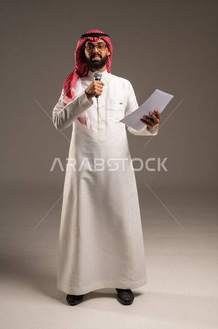 إعداد وتحضير أفكار الخطاب بشكل مسبق، القيام بالحوارات والنقاشات، بورتريه لرجل عربي خليجي سعودي يرتدي الثوب التقليدي والشماغ يحمل بيده مجموعة من الأوراق ومكبر الصوت يقوم بإلقاء الخطابات وينظر إلى الكاميرا، صورة الجسم بالطول الكامل، خلفية رمادية