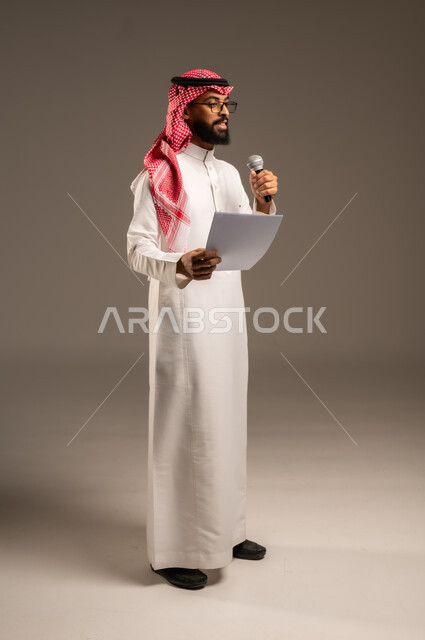 القيام بالحوارات والنقاشات، قراءة الملاحظات والمعلومات، بورتريه لرجل عربي خليجي سعودي يرتدي الثوب التقليدي والشماغ يحمل بيده مجموعة من الأوراق ومكبر الصوت يقوم بإلقاء الخطابات، إعداد وتحضير أفكار الخطاب بشكل مسبق،صورة الجسم بالطول الكامل، خلفية رمادية