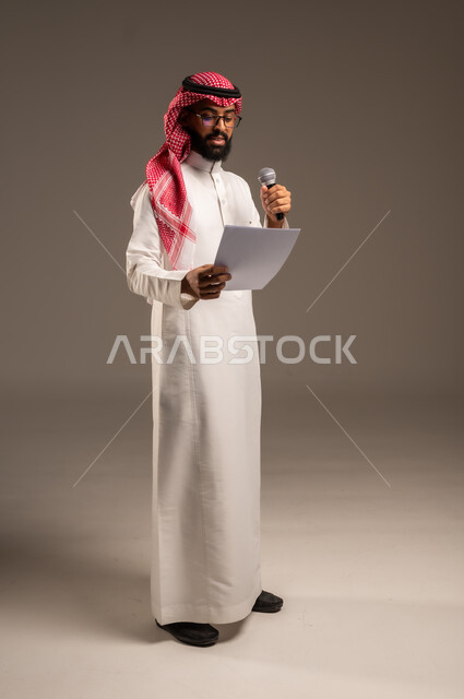 القيام بالحوارات والنقاشات، قراءة الملاحظات والمعلومات، بورتريه لرجل عربي خليجي سعودي يرتدي الثوب التقليدي والشماغ يحمل بيده مجموعة من الأوراق ومكبر الصوت يقوم بإلقاء الخطابات، إعداد وتحضير أفكار الخطاب بشكل مسبق،صورة الجسم بالطول الكامل، خلفية رمادية