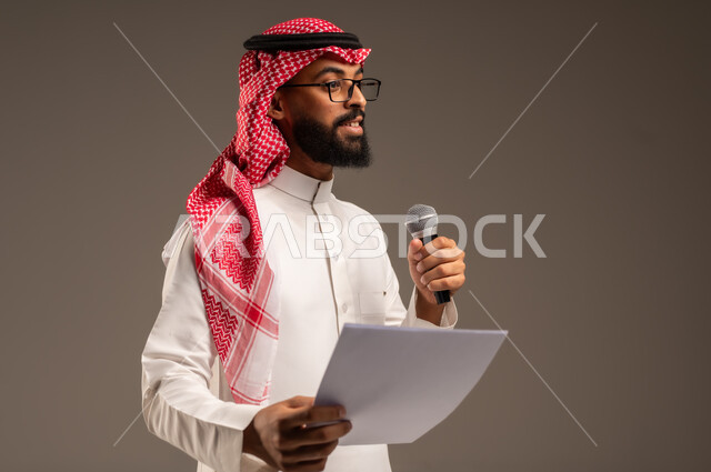 قراءة الملاحظات والمعلومات، بورتريه مقرب لرجل عربي خليجي سعودي يرتدي الثوب التقليدي والشماغ يحمل بيده مجموعة من الأوراق ومكبر الصوت يقوم بإلقاء الخطابات، القيام بالحوارات والنقاشات، إعداد وتحضير أفكار الخطاب بشكل مسبق، خلفية رمادية