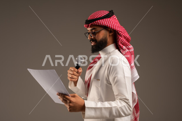 القيام بالحوارات والنقاشات، قراءة الملاحظات والمعلومات، بورتريه مقرب من الجانب لرجل عربي خليجي سعودي يرتدي الثوب التقليدي والشماغ يحمل بيده مجموعة من الأوراق ومكبر الصوت يقوم بإلقاء الخطابات، إعداد وتحضير أفكار الخطاب بشكل مسبق، خلفية رمادية