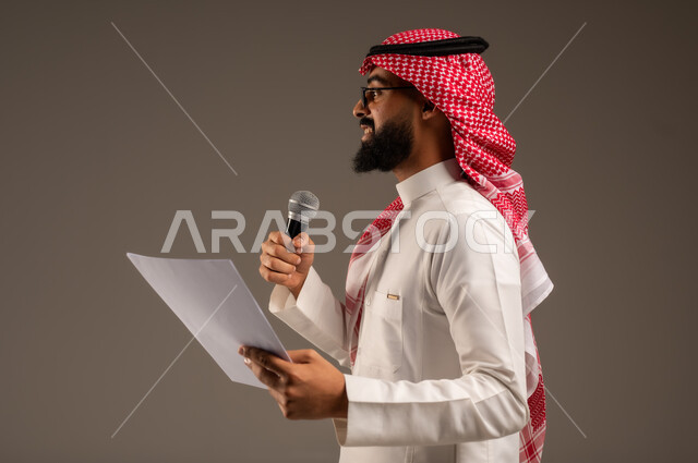 Conducting dialogues and discussions, reading notes and information, close-up side portrait of a Saudi Arabian Gulf man wearing traditional thobe and shemagh holding a stack of papers and a loudspeaker giving speeches, preparing and arranging speech ideas in advance, gray background