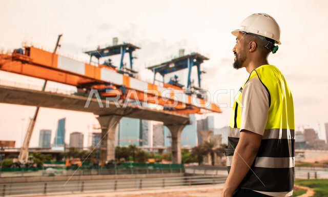 إنشاء الأساسات والهياكل للمشروعات السكنية، أعمال البناء والمقاولات والتطوير العقاري في السعودية، مهندس معماري عربي خليجي سعودي يرتدي الخوذة وسترة الحماية يقف في موقع البناء، تشييد المباني والمشاريع الضخمة