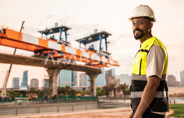 إنشاء الأساسات والهياكل للمشروعات السكنية، أعمال البناء والمقاولات والتطوير العقاري في السعودية، مهندس معماري عربي خليجي سعودي يرتدي الخوذة وسترة الحماية يقف في موقع البناء، تشييد المباني والمشاريع الضخمة