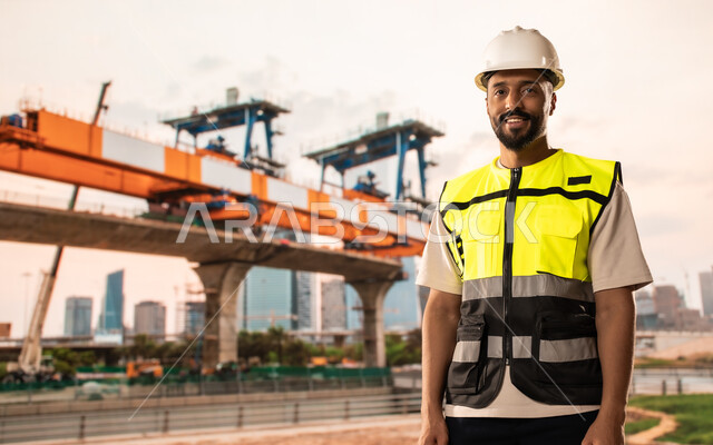 إنشاء الأساسات والهياكل للمشروعات السكنية، أعمال البناء والمقاولات والتطوير العقاري في السعودية، مهندس معماري عربي خليجي سعودي يرتدي الخوذة وسترة الحماية يقف في موقع البناء، تشييد المباني والمشاريع الضخمة