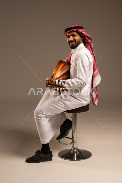 ممارسة الهوايات الفنية، فنان يقدم البرامج والفنون الموسيقية والفن المسرحي، مواهب فنية موسيقية، بورتريه لرجل خليجي سعودي عربي يرتدي الثوب التقليدي والشماغ يعزف على الة العود، الإستمتاع بالعزف على الآلات الوترية الكلاسيكية، جلسة وناسة وطرب، خلفية رمادية