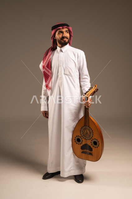 ممارسة الهوايات الفنية، فنان يقدم البرامج والفنون الموسيقية والفن المسرحي، مواهب فنية موسيقية، بورتريه لرجل خليجي سعودي عربي يرتدي الثوب التقليدي والشماغ يعزف على الة العود، الإستمتاع بالعزف على الآلات الوترية الكلاسيكية، جلسة وناسة وطرب، خلفية رمادية