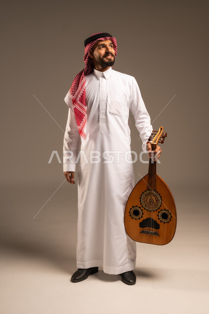 ممارسة الهوايات الفنية، فنان يقدم البرامج والفنون الموسيقية والفن المسرحي، مواهب فنية موسيقية، بورتريه لرجل خليجي سعودي عربي يرتدي الثوب التقليدي والشماغ يعزف على الة العود، الإستمتاع بالعزف على الآلات الوترية الكلاسيكية، جلسة وناسة وطرب، خلفية رمادية