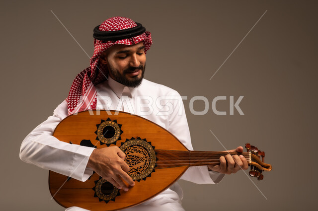 الإستمتاع بالعزف على الآلات الوترية الكلاسيكية، جلسة وناسة وطرب، ممارسة الهوايات الفنية، فنان يقدم البرامج والفنون الموسيقية والفن المسرحي، مواهب فنية موسيقية، بورتريه لرجل خليجي سعودي عربي يرتدي الثوب التقليدي والشماغ يعزف على الة العود، خلفية رمادية
