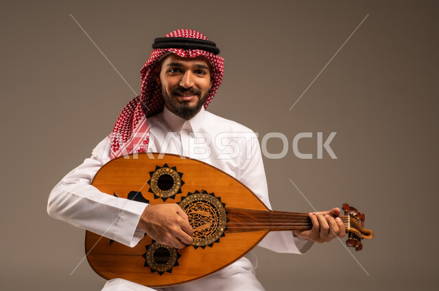 الإستمتاع بالعزف على الآلات الوترية الكلاسيكية، جلسة وناسة وطرب، ممارسة الهوايات الفنية، فنان يقدم البرامج والفنون الموسيقية والفن المسرحي، مواهب فنية موسيقية، بورتريه لرجل خليجي سعودي عربي يرتدي الثوب التقليدي والشماغ يعزف على الة العود، خلفية رمادية