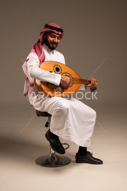 جلسة وناسة وطرب، ممارسة الهوايات الفنية، فنان يقدم البرامج والفنون الموسيقية والفن المسرحي، مواهب فنية موسيقية، بورتريه لرجل خليجي سعودي عربي يرتدي الثوب التقليدي والشماغ يعزف على الة العود، الإستمتاع بالعزف على الآلات الوترية الكلاسيكية، خلفية رمادية
