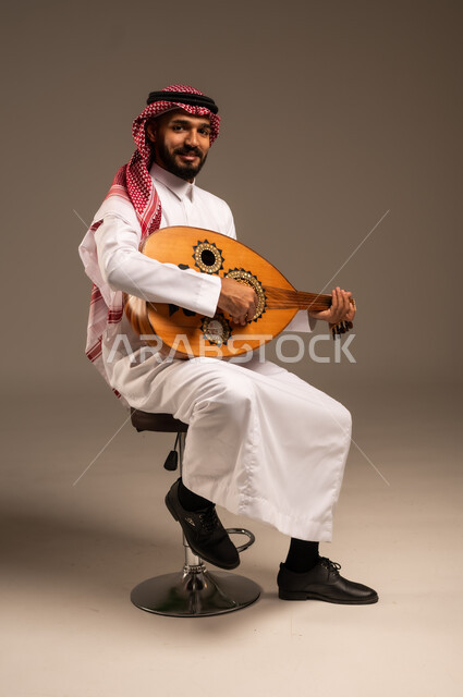 جلسة وناسة وطرب، ممارسة الهوايات الفنية، فنان يقدم البرامج والفنون الموسيقية والفن المسرحي، مواهب فنية موسيقية، بورتريه لرجل خليجي سعودي عربي يرتدي الثوب التقليدي والشماغ يعزف على الة العود، الإستمتاع بالعزف على الآلات الوترية الكلاسيكية، خلفية رمادية
