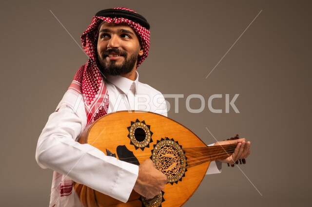 الإستمتاع بالعزف على الآلات الوترية الكلاسيكية، جلسة وناسة وطرب، ممارسة الهوايات الفنية، فنان يقدم البرامج والفنون الموسيقية والفن المسرحي، مواهب فنية موسيقية، بورتريه لرجل خليجي سعودي عربي يرتدي الثوب التقليدي والشماغ يعزف على الة العود، خلفية رمادية