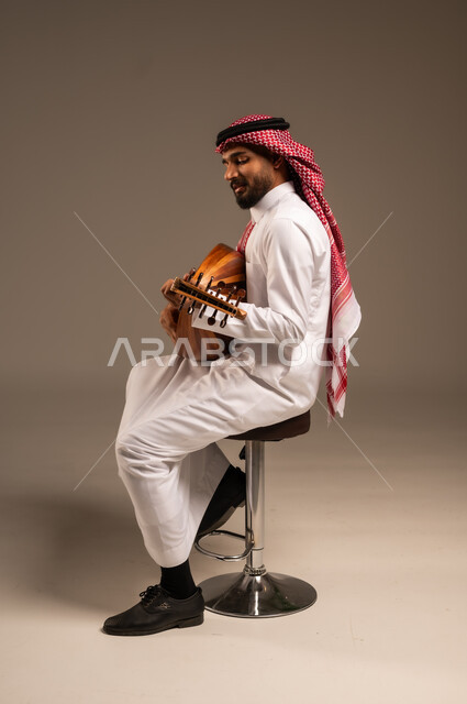 الإستمتاع بالعزف على الآلات الوترية الكلاسيكية، جلسة وناسة وطرب، ممارسة الهوايات الفنية، فنان يقدم البرامج والفنون الموسيقية والفن المسرحي، مواهب فنية موسيقية، بورتريه لرجل خليجي سعودي عربي يرتدي الثوب التقليدي والشماغ يعزف على الة العود، خلفية رمادية