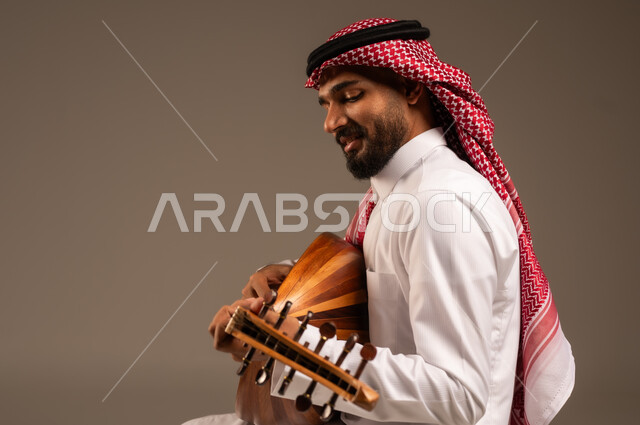 الإستمتاع بالعزف على الآلات الوترية الكلاسيكية، جلسة وناسة وطرب، ممارسة الهوايات الفنية، فنان يقدم البرامج والفنون الموسيقية والفن المسرحي، مواهب فنية موسيقية، بورتريه لرجل خليجي سعودي عربي يرتدي الثوب التقليدي والشماغ يعزف على الة العود، خلفية رمادية