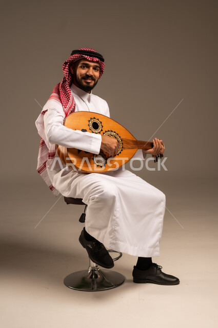 Enjoying playing classical stringed instruments, a fun and singing session, practicing artistic hobbies, an artist presenting programs, musical arts and theatrical art, musical artistic talents, a portrait of a Saudi Arabian Gulf man wearing traditional thobe and shemagh playing the oud, gray background