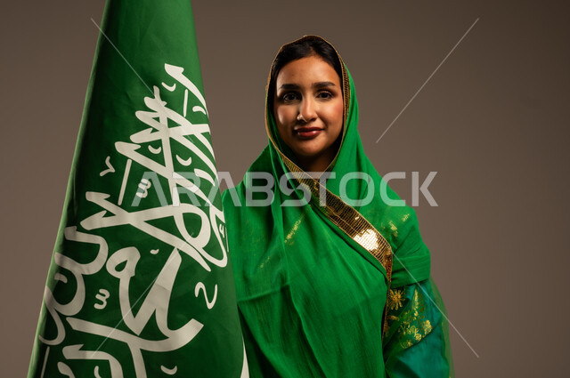 المشاركة بالأعياد الوطنية، اليوم الوطني السعودي، بورتريه لامرأة عربية خليجية سعودية محجبة  ترتدي الشيلة والبشت وترفع علم السعودية بايماءات الفخر والاعتزاز بالوطن، يوم العلم السعودي 11 مارس، العيد الوطني 23 سبتمبر، خلفية بيج