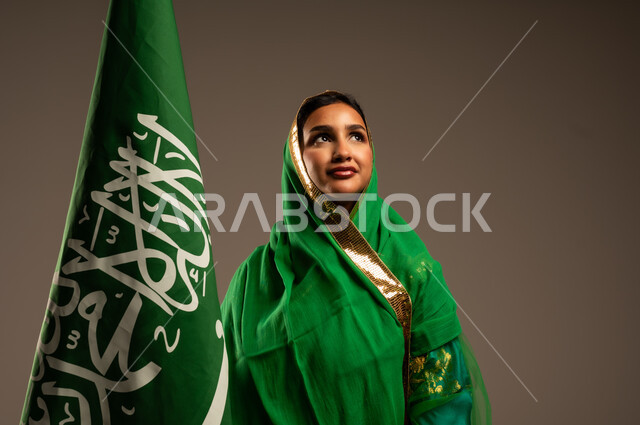 المشاركة بالأعياد الوطنية، اليوم الوطني السعودي، بورتريه لامرأة عربية خليجية سعودية محجبة  ترتدي الشيلة والبشت وترفع علم السعودية بايماءات الفخر والاعتزاز بالوطن، يوم العلم السعودي 11 مارس، العيد الوطني 23 سبتمبر، خلفية بيج
