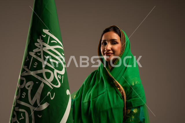 المشاركة بالأعياد الوطنية، اليوم الوطني السعودي، بورتريه لامرأة عربية خليجية سعودية محجبة  ترتدي الشيلة والبشت وترفع علم السعودية بايماءات الفخر والاعتزاز بالوطن، يوم العلم السعودي 11 مارس، العيد الوطني 23 سبتمبر، خلفية بيج