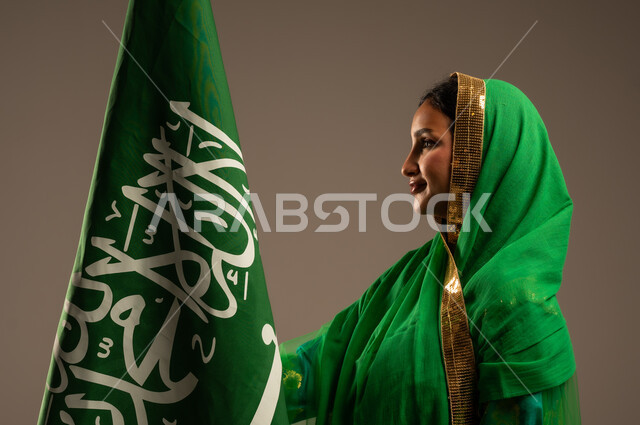 المشاركة بالأعياد الوطنية، اليوم الوطني السعودي، بورتريه لامرأة عربية خليجية سعودية محجبة  ترتدي الشيلة والبشت وترفع علم السعودية بايماءات الفخر والاعتزاز بالوطن، يوم العلم السعودي 11 مارس، العيد الوطني 23 سبتمبر، خلفية بيج