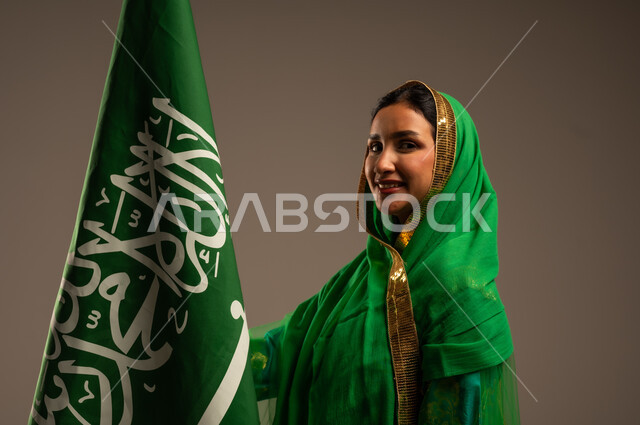 المشاركة بالأعياد الوطنية، اليوم الوطني السعودي، بورتريه لامرأة عربية خليجية سعودية محجبة  ترتدي الشيلة والبشت وترفع علم السعودية بايماءات الفخر والاعتزاز بالوطن، يوم العلم السعودي 11 مارس، العيد الوطني 23 سبتمبر، خلفية بيج