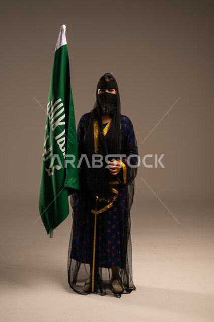  ذكرى تأسيس الدولة السعودية الأولى 22 فبراير، يوم بدينا 1727 م، بورتريه لإمرأة عربية خليجية سعودية ترتدي زي المنطقة الوسطى وتمسك بيدها علم التأسيس, الاعتزاز بالبلد والانتماء اليه، الجسم بالطول الكامل، خلفية بيج