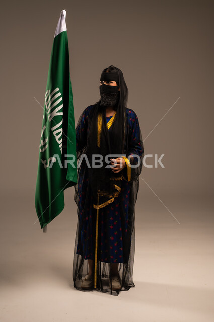  ذكرى تأسيس الدولة السعودية الأولى 22 فبراير، يوم بدينا 1727 م، بورتريه لإمرأة عربية خليجية سعودية ترتدي زي المنطقة الوسطى وتمسك بيدها علم التأسيس, الاعتزاز بالبلد والانتماء اليه، الجسم بالطول الكامل، خلفية بيج