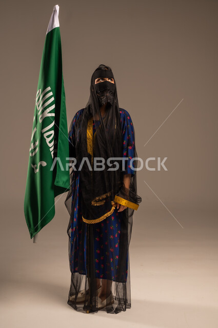  ذكرى تأسيس الدولة السعودية الأولى 22 فبراير، يوم بدينا 1727 م، بورتريه لإمرأة عربية خليجية سعودية ترتدي زي المنطقة الوسطى وتمسك بيدها علم التأسيس, الاعتزاز بالبلد والانتماء اليه، الجسم بالطول الكامل، خلفية بيج