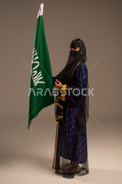  ذكرى تأسيس الدولة السعودية الأولى 22 فبراير، يوم بدينا 1727 م، بورتريه لإمرأة عربية خليجية سعودية ترتدي زي المنطقة الوسطى وتمسك بيدها علم التأسيس, الاعتزاز بالبلد والانتماء اليه، الجسم بالطول الكامل، خلفية بيج