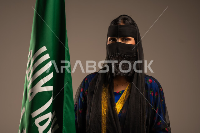 يوم بدينا 1727 م، ذكرى تأسيس الدولة السعودية الأولى 22 فبراير، اليوم الوطني السعودي، بورتريه لإمرأة عربية خليجية سعودية ترتدي زي المنطقة الوسطى وتمسك بيدها علم التأسيس, الاعتزاز بالبلد والانتماء اليه، خلفية بيج