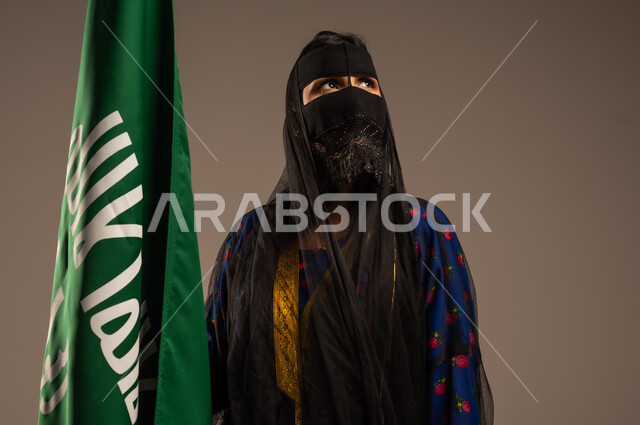 يوم بدينا 1727 م، ذكرى تأسيس الدولة السعودية الأولى 22 فبراير، اليوم الوطني السعودي، بورتريه لإمرأة عربية خليجية سعودية ترتدي زي المنطقة الوسطى وتمسك بيدها علم التأسيس, الاعتزاز بالبلد والانتماء اليه، خلفية بيج