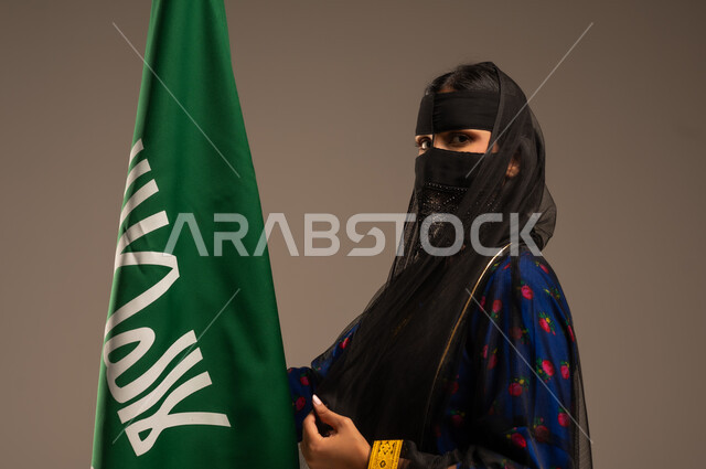 يوم بدينا 1727 م، ذكرى تأسيس الدولة السعودية الأولى 22 فبراير، اليوم الوطني السعودي، بورتريه لإمرأة عربية خليجية سعودية ترتدي زي المنطقة الوسطى وتمسك بيدها علم التأسيس, الاعتزاز بالبلد والانتماء اليه، خلفية بيج