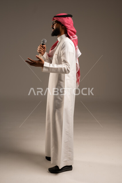 تقديم الأفكار ومناقشتها، تبادل الحوارات والتواصل الفعال، بورتريه من الجانب لرجل عربي خليجي سعودي يرتدي الثوب التقليدي والشماغ يحمل بيده مكبر الصوت يقوم بإلقاء الخطابات، إجراء المقابلات وطرح الأسئلة، صورة الجسم بالطول الكامل، خلفية رمادية