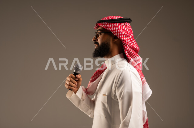 تقديم الأفكار ومناقشتها، تبادل الحوارات والتواصل الفعال، بورتريه مقرب من الجانب لرجل عربي خليجي سعودي يرتدي الثوب التقليدي والشماغ يحمل بيده مكبر الصوت يقوم بإلقاء الخطابات، إجراء المقابلات وطرح الأسئلة، خلفية رمادية